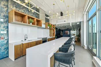 A long kitchen with a long white counter and chairs